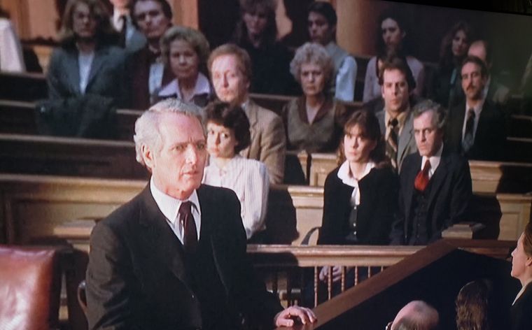 Un jovencísimo Bruce Willis (de camisa color mostaza y corbata a rayas), observa a Paul Newman defendiendo su caso desde el estrado. Un jovencísimo Bruce Willis (de camisa color mostaza y corbata a rayas), observa a Paul Newman defendiendo su caso desde el estrado.